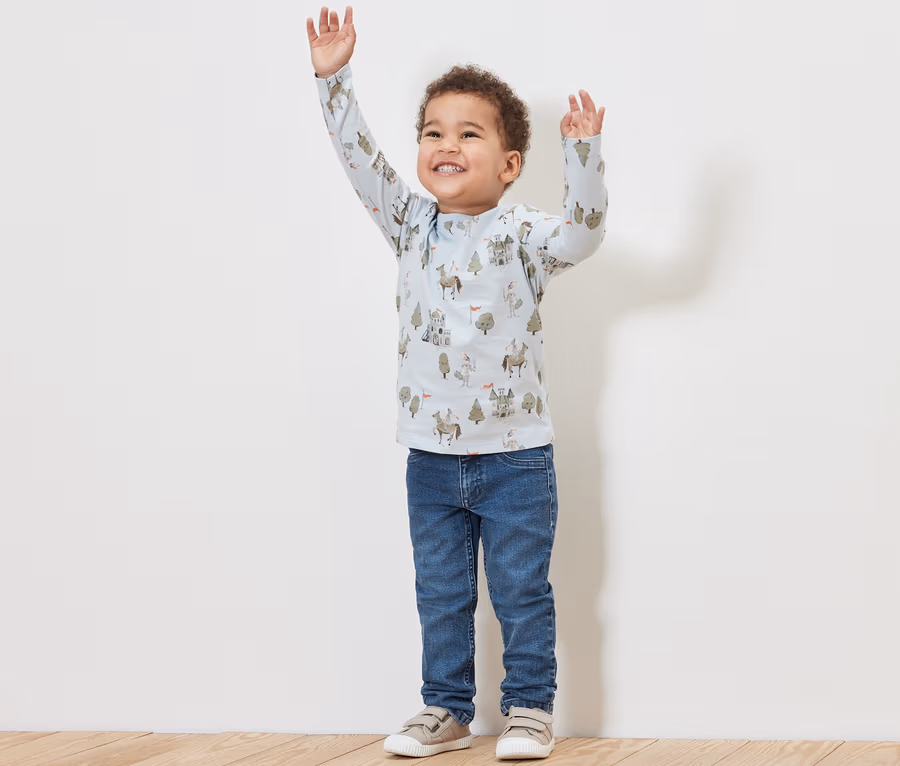 Junge mit erhobenen Armen trägt Kinder-Jeans – Fit »Jonas« und ein bedrucktes Shirt.