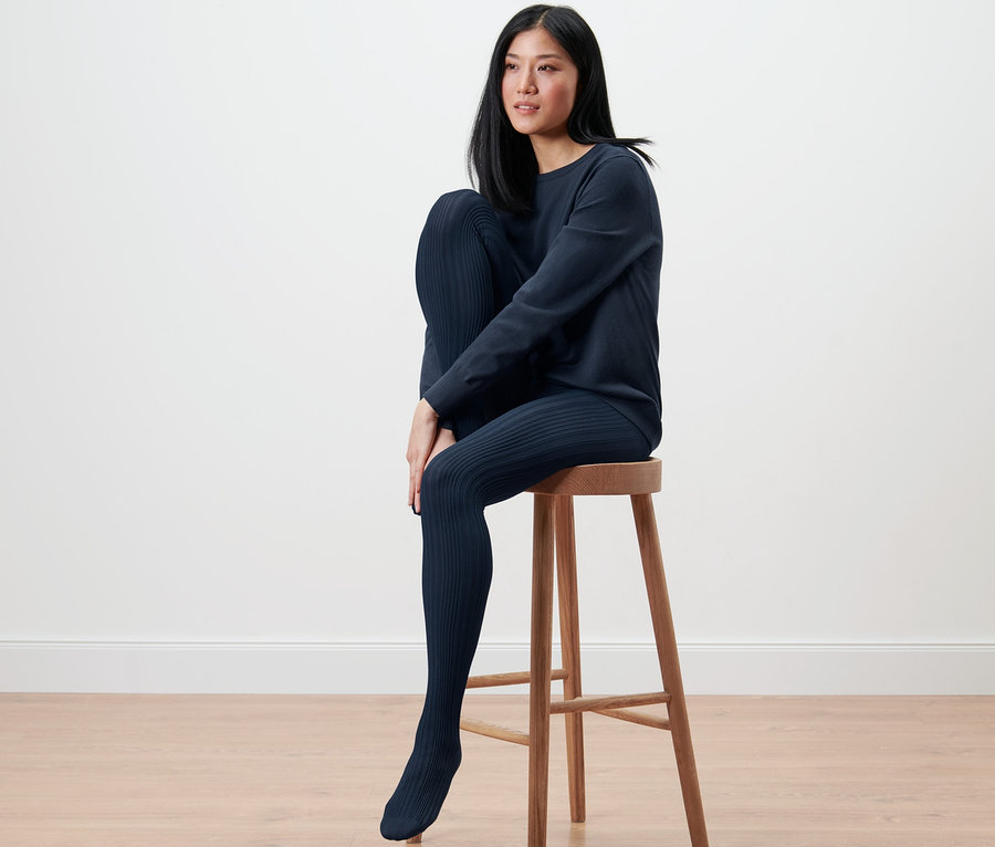 Frau sitzt auf einem Hocker und trägt eine gemusterte Feinstrumpfhose.