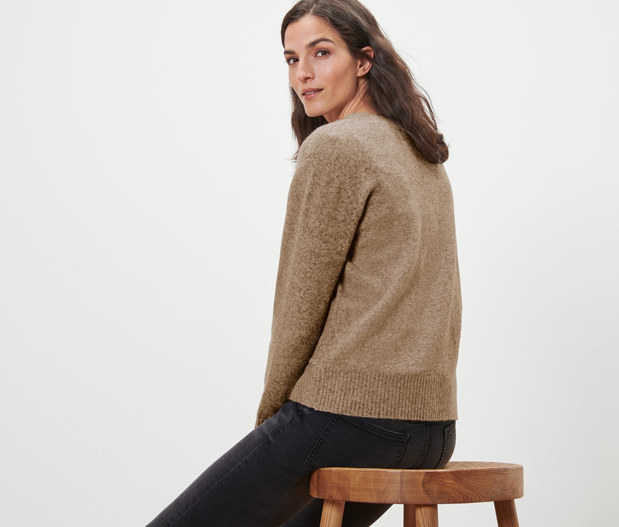 Frau sitzt auf einem Holzhocker und trägt eine Strickjacke mit Wolle.