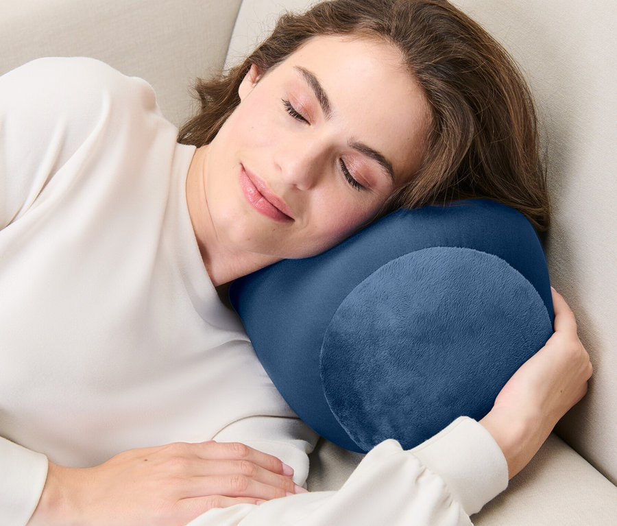 Frau schläft auf einem beigen Sofa mit einem Relaxkissen.