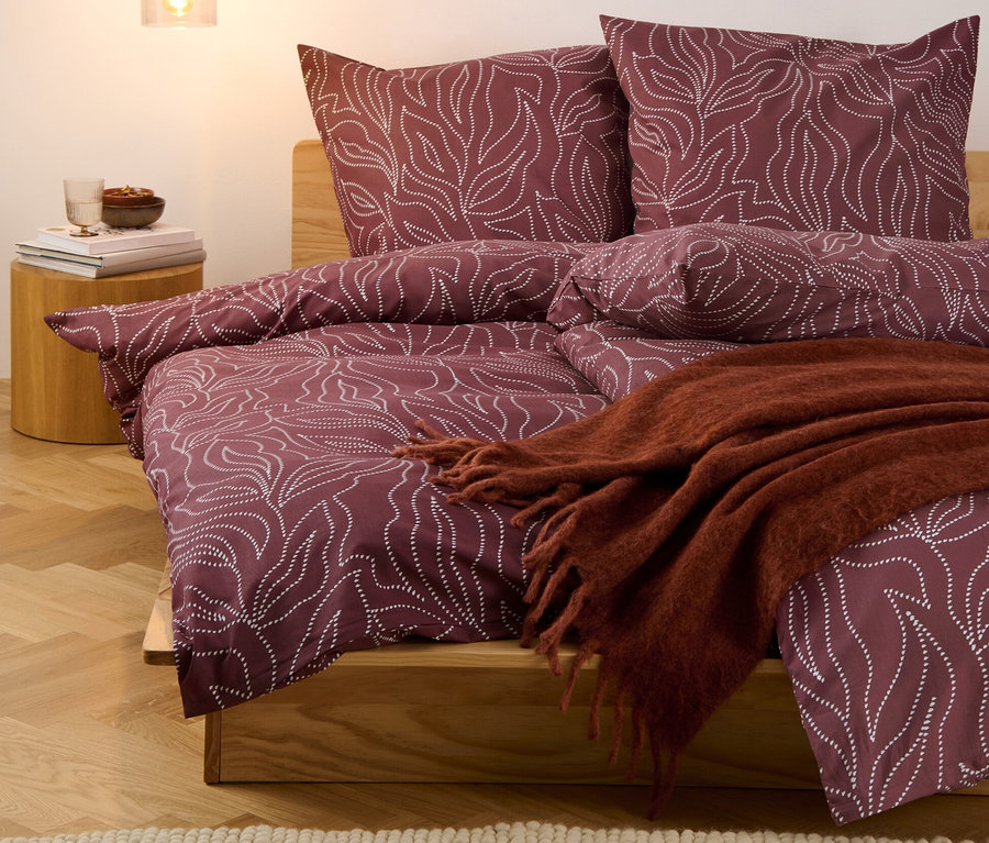 Ein Bett mit bordeauxfarbener Renforcé-Bettwäsche mit Blattmuster, inklusive drei Sets Renforcé-Bettwäsche in Normalgröße und einem Set in Übergröße.