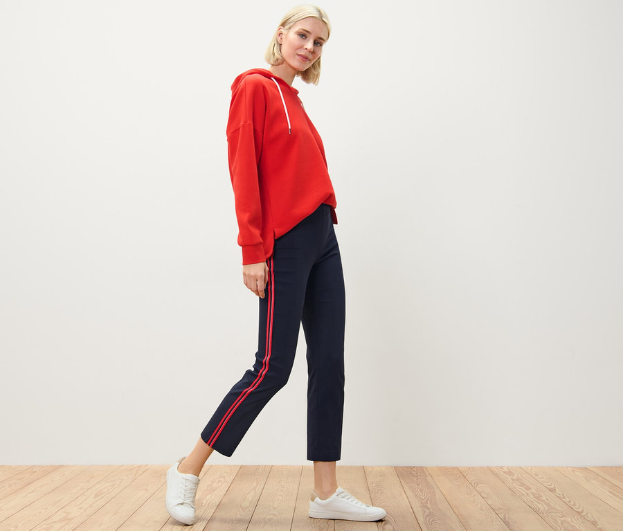 Blonde Frau posiert in rotem Hoodie und Stretchhose mit Galonstreifen.