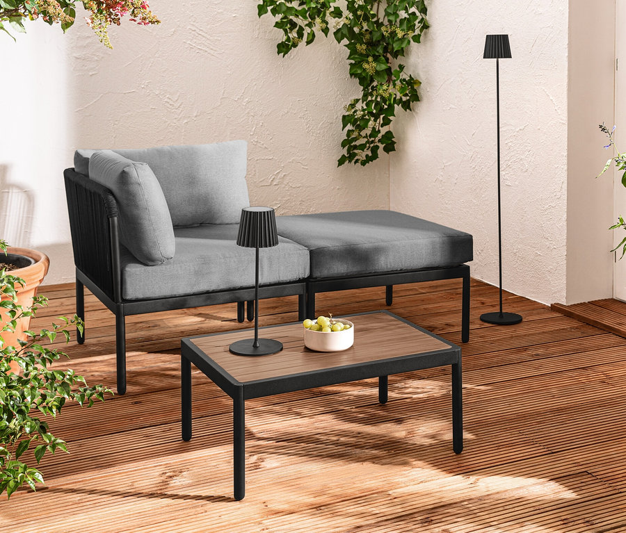 Terrasse mit modularer Lounge mit Textilgeflecht, schwarzer LED-Akku-Outdoor-Tischleuchte und Stehleuchte, sowie LED-Filament-Lichterkette.