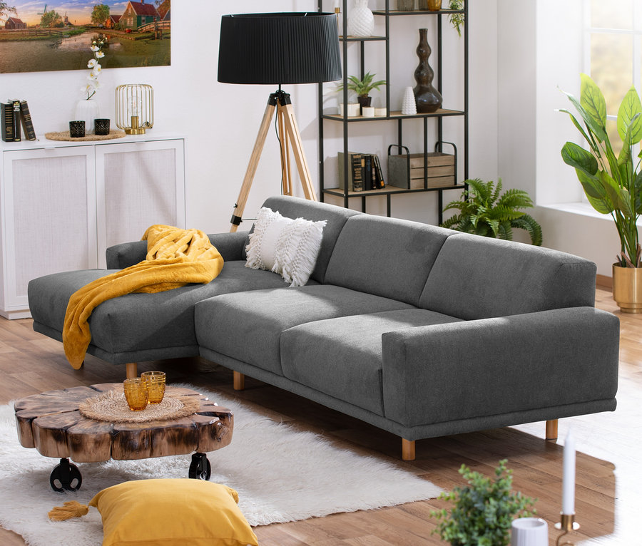 Wohnzimmer mit dunkelgrauem Ecksofa »Penelope« links, einem Couchtisch aus Holz und Dekorationen.