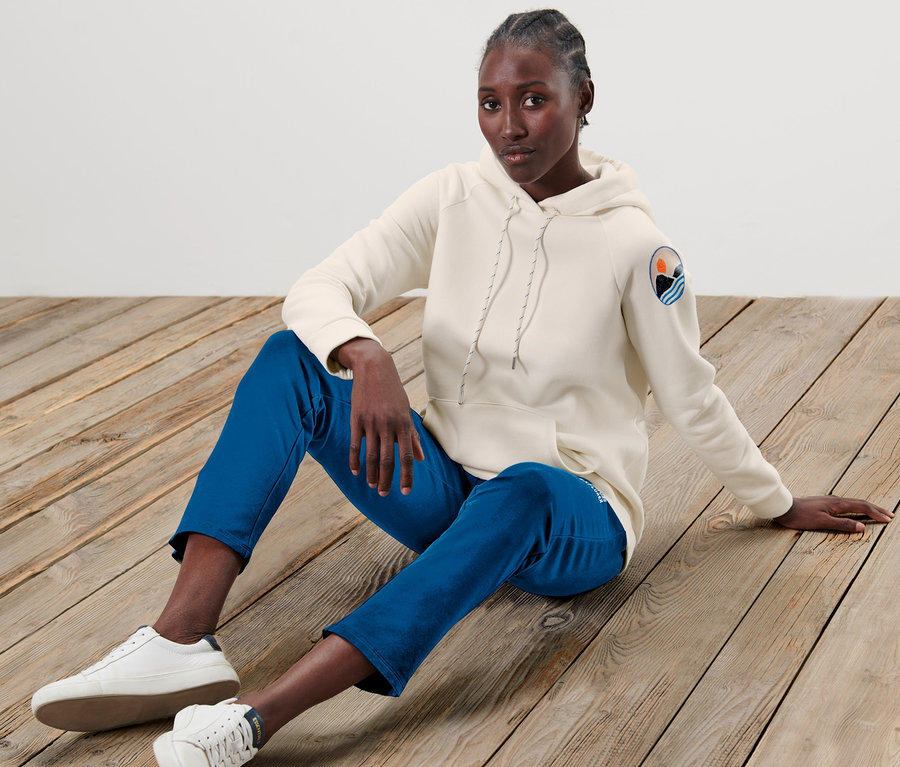 Frau sitzt auf Holzboden und trägt ein beiges Kapuzensweatshirt.