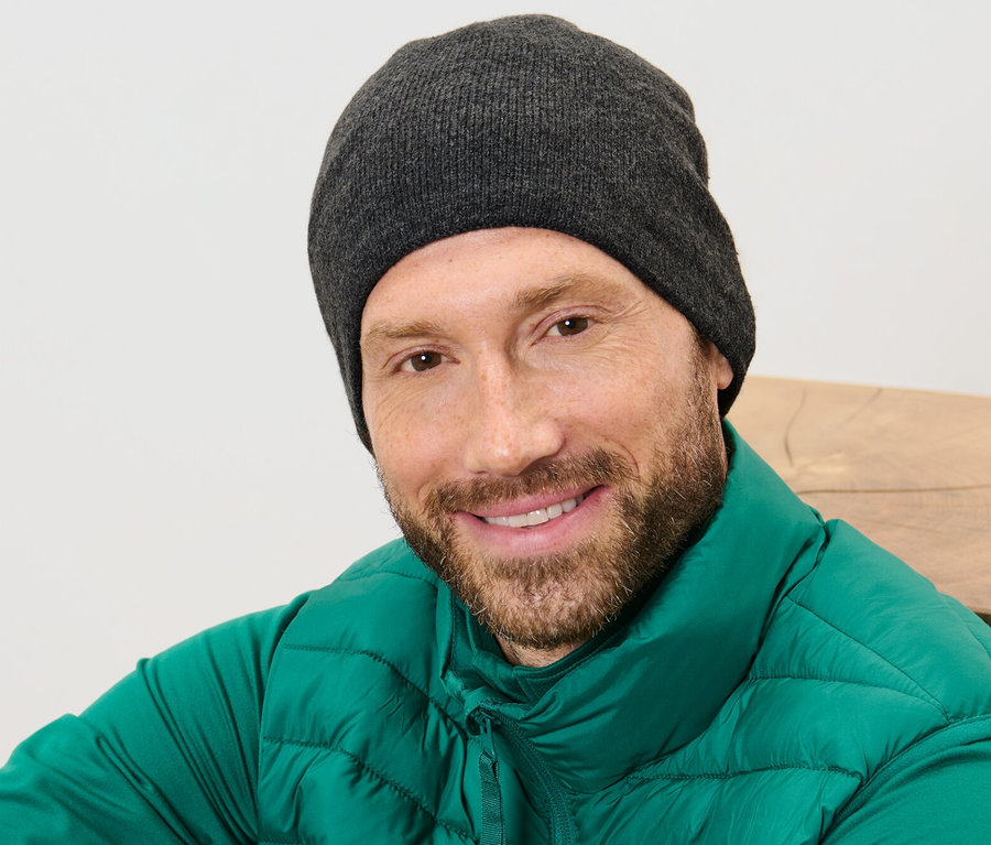 Mann mit Bart lächelt, trägt eine Strickmütze und eine grüne Weste.