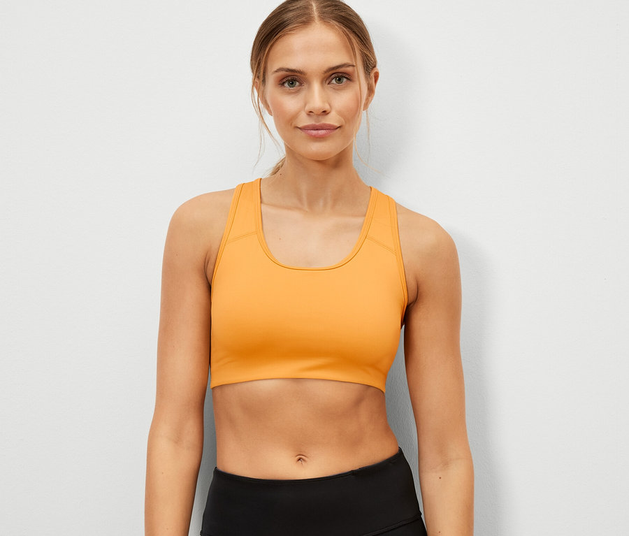 Frau trägt einen orangefarbenen Sport-Bustier aus einem 2er-Set.