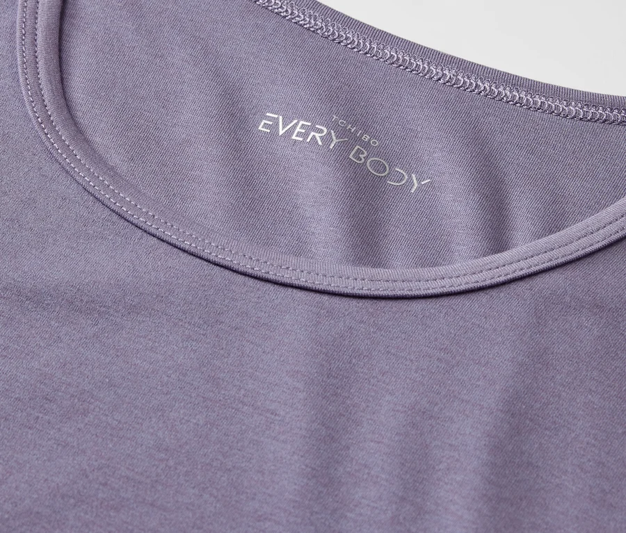 Detailaufnahme eines lila T-Shirts mit Rundhalsausschnitt und dem Aufdruck "EVERY BODY".