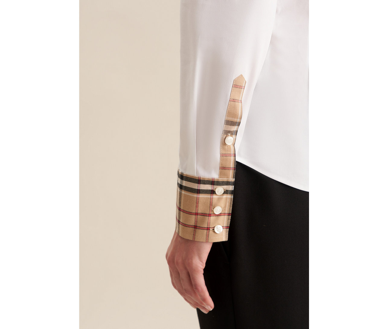 Nahaufnahme eines Arms in einer weißen Seidensticker Popeline-Bluse mit Karodetail an Manschette und Knopfleiste. Die Manschette ist umgeschlagen und zeigt das beige, schwarze und rote Karomuster sowie weiße Knöpfe.