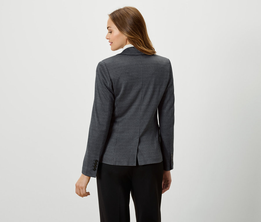 Eine Frau trägt einen Blazer mit Karomuster und eine schwarze Hose.