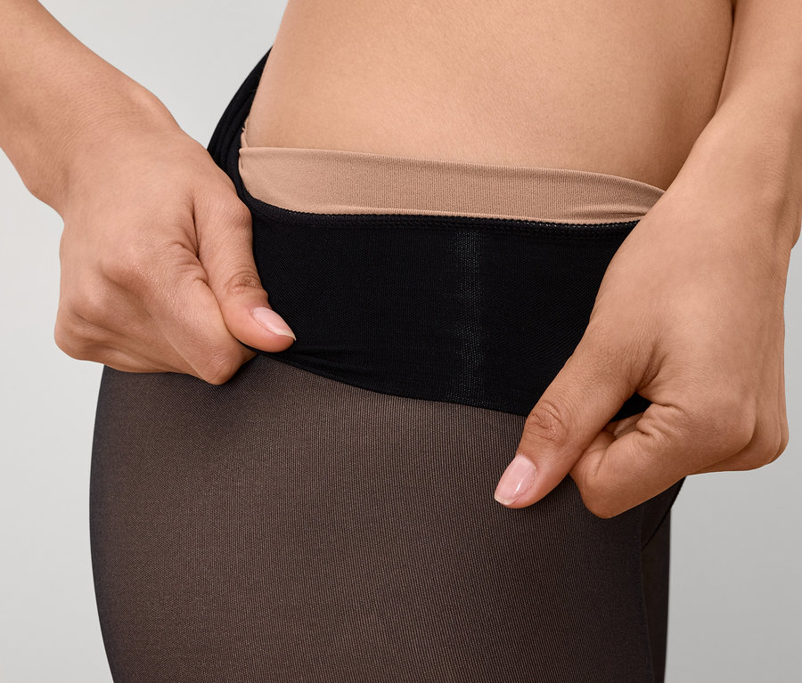 Detailaufnahme einer Frau, die eine schwarze Strumpfhose mit nudefarbenem Bund hochzieht.
