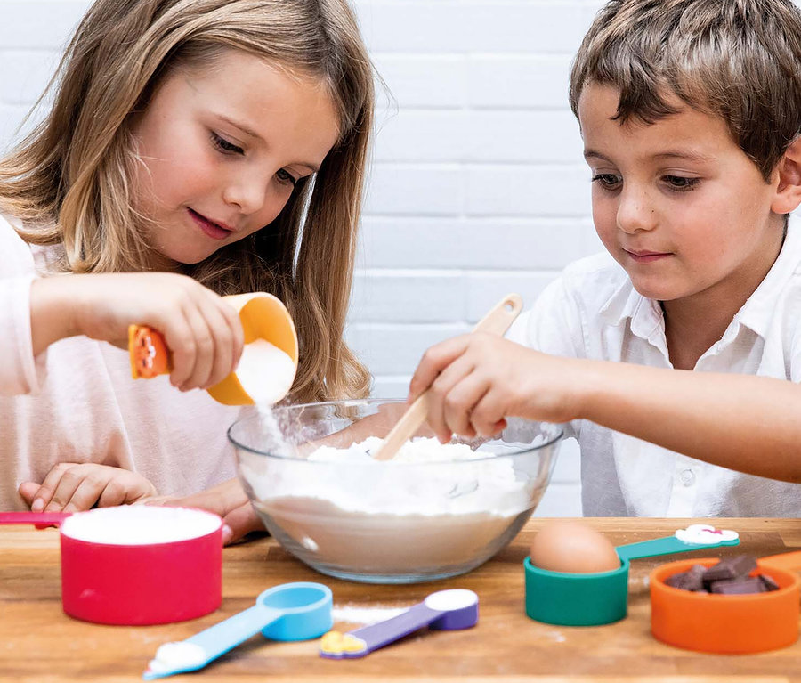 Kinder benutzen Messbecher aus dem Chefclub Koch-Set, um Zutaten in eine Schüssel zu geben.