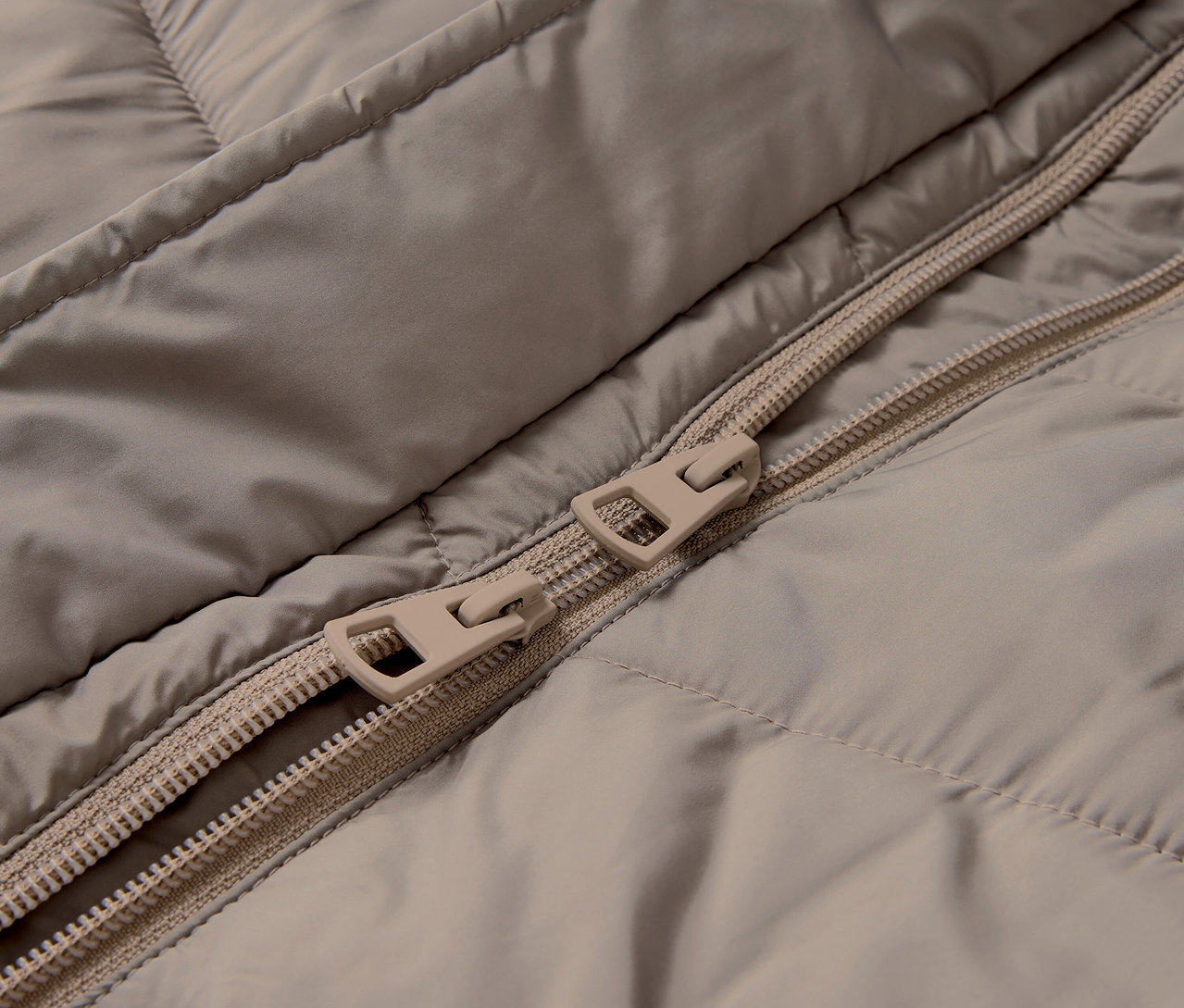 Detailaufnahme einer beige gesteppten Jacke mit Reißverschluss.