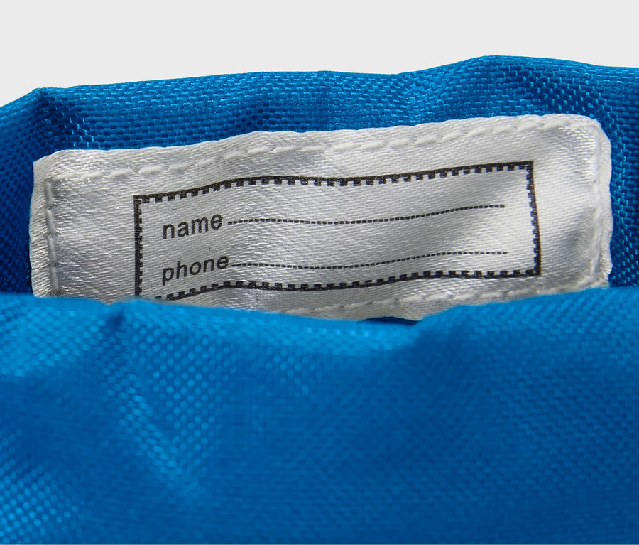 Auf blauem Stoff ist ein weißes Etikett mit einem schwarzen Rahmen für Name und Telefon aufgenäht.