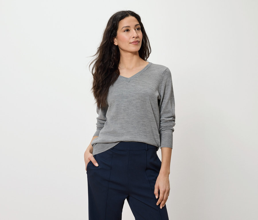 Frau posiert in grauem Langarmpullover und dunkelblauer Hose.