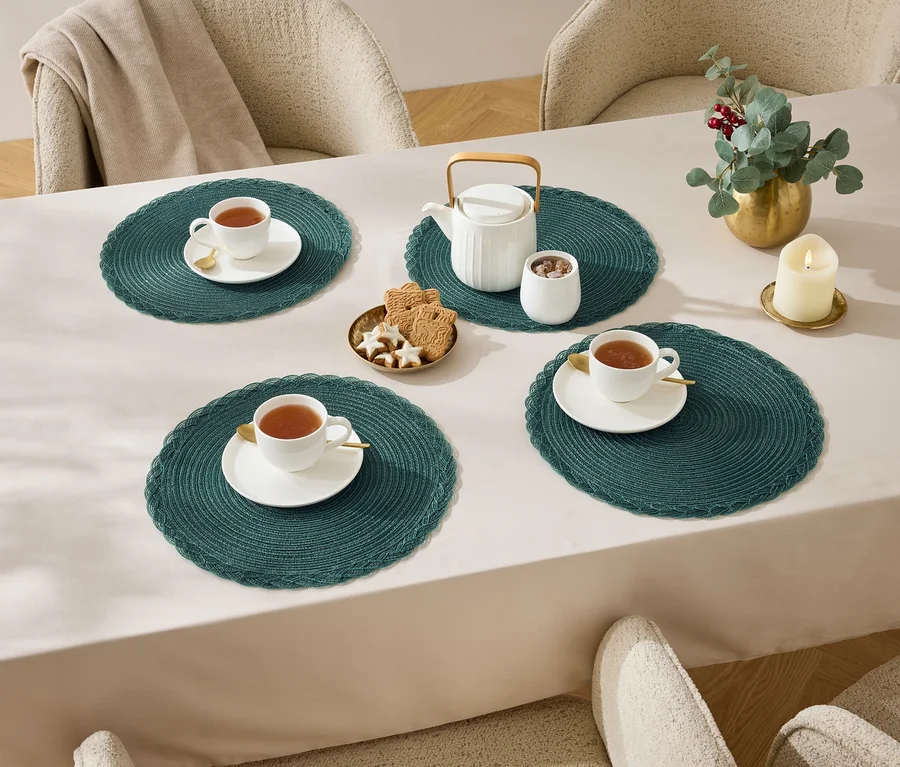Vier Tassen Tee auf einem Tisch mit einer Tischdecke, Teekanne, Zuckerdose, Kekse und einer Kerze.