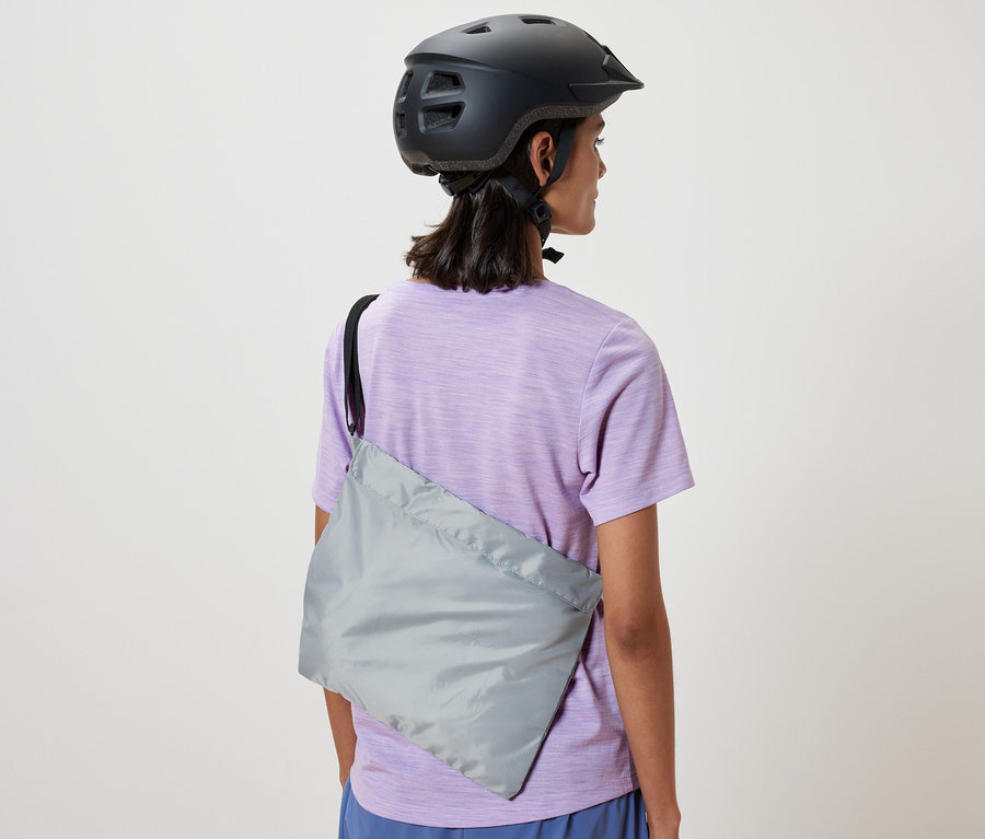 Frau mit Fahrradhelm hat eine Fahrrad-Einkaufstasche über der Schulter.