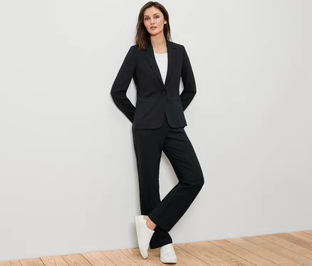 Frau posiert in schwarzem Jerseyblazer, schwarzer Hose und weißen Turnschuhen.