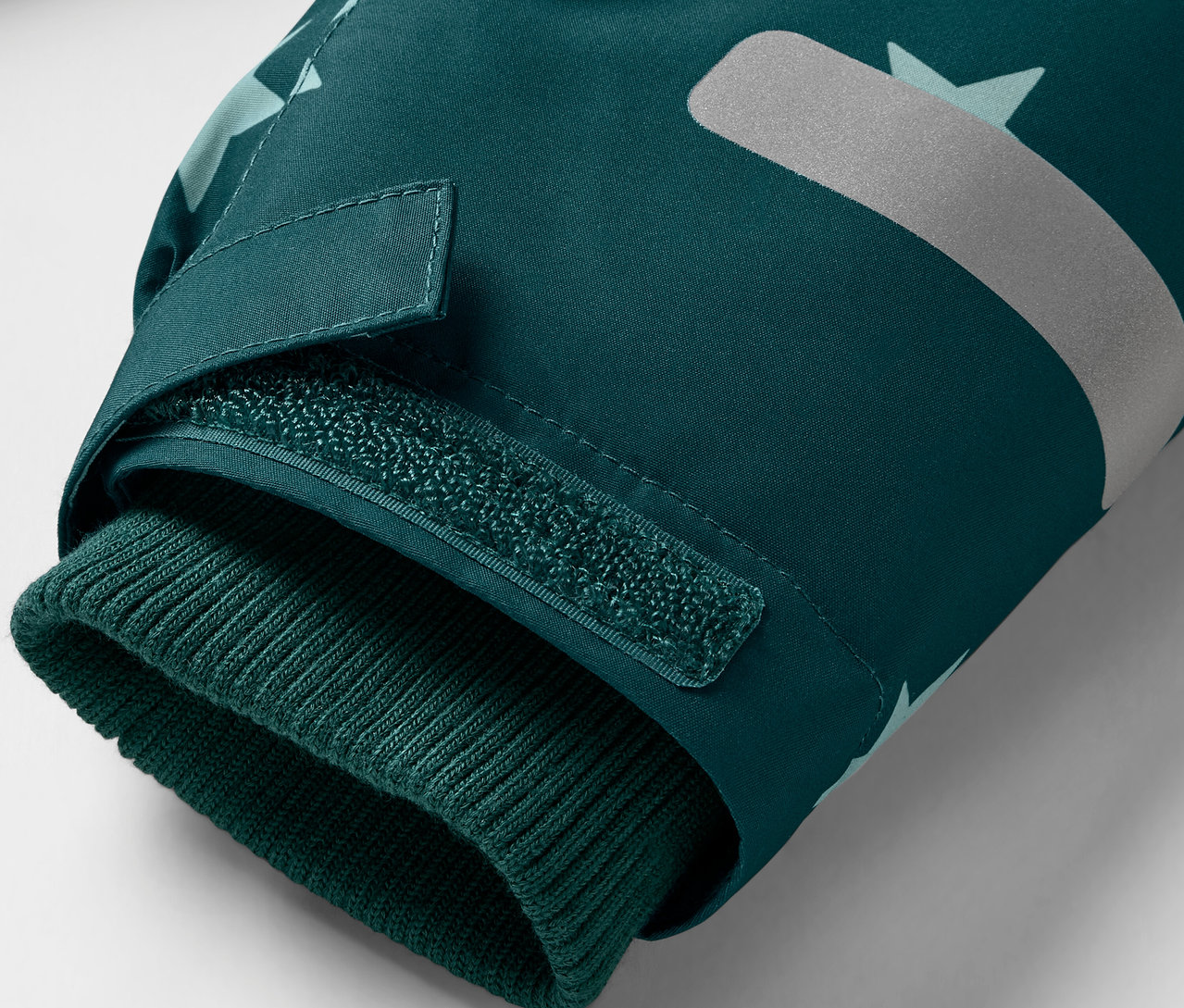 Detailansicht einer dunkelgrünen Jacke mit Strickbündchen und Reflektor.