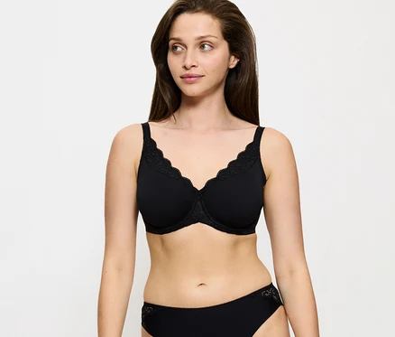 Eine Frau trägt einen schwarzen Triumph Amourette Minimizer-BH mit Spitzenbesatz und einen passenden schwarzen Slip und blickt zur Seite.