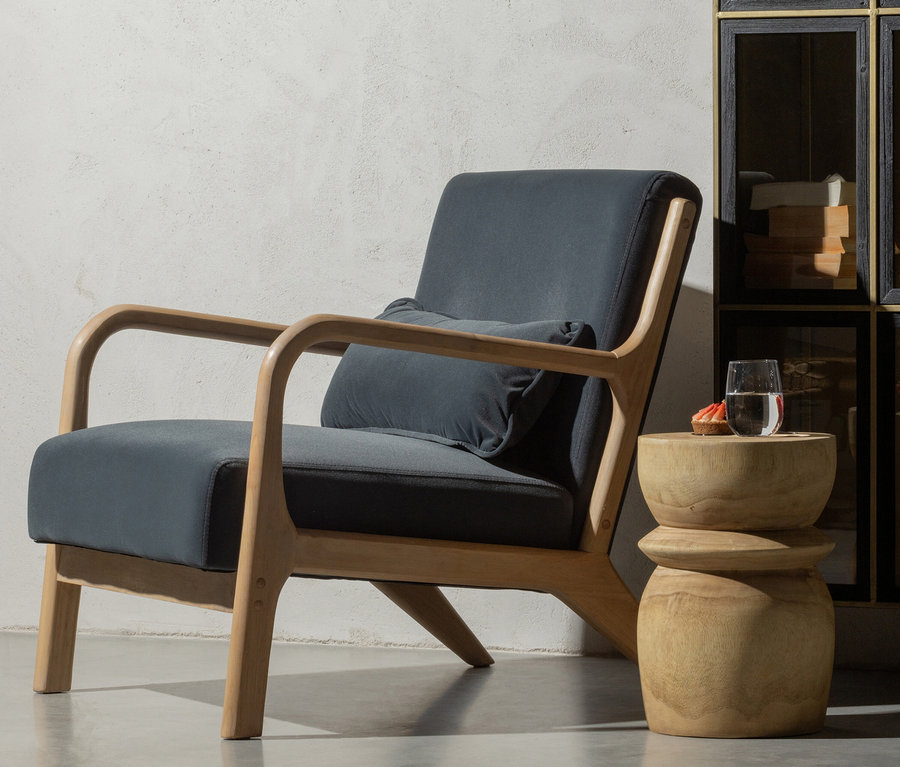 Grauer Sessel mit Holzarmlehnen und ein brauner Holzhocker Woood Hocker »Bikkel« mit Wasser und Gebäck.