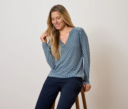 Frau sitzt auf einem Hocker, trägt ein blau-weiß gestreiftes Langarmshirt und dunkelblaue Hosen.