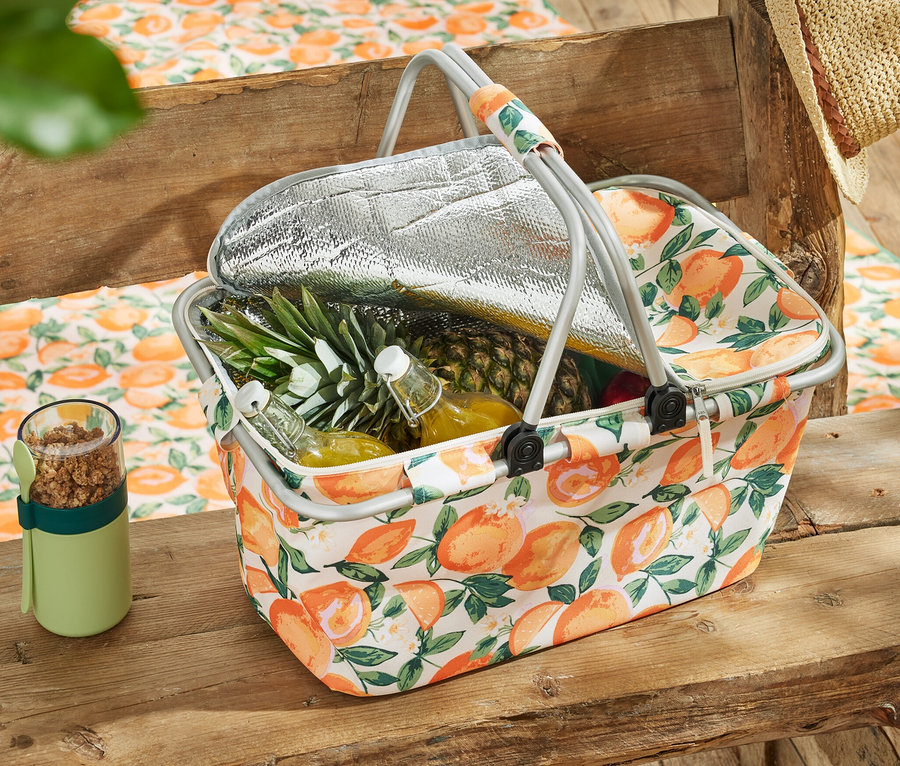 Kühlkorb mit Obst und Getränken auf einem Holztisch.