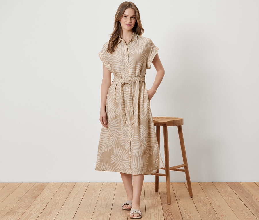 Frau steht neben einem Holzhocker und trägt ein bedrucktes Leinenkleid.