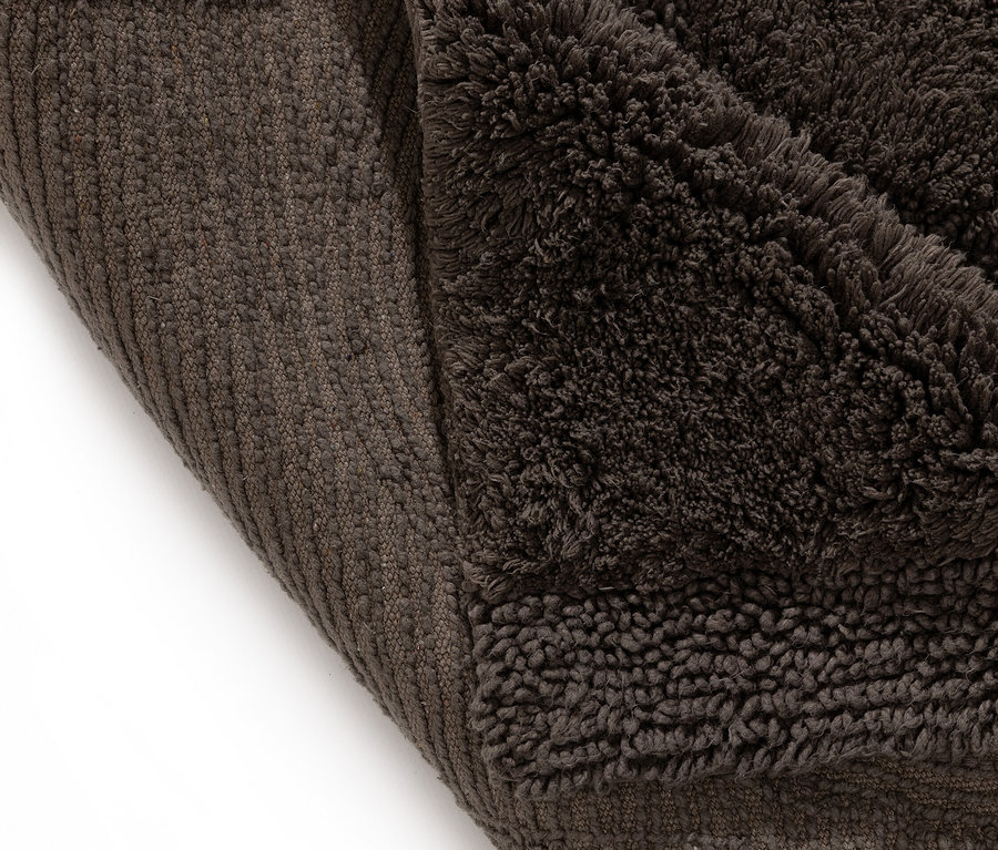 Nahaufnahme einer dunkelbraunen Badematte, die an einer Ecke umgeschlagen ist und die Unterseite zeigt.