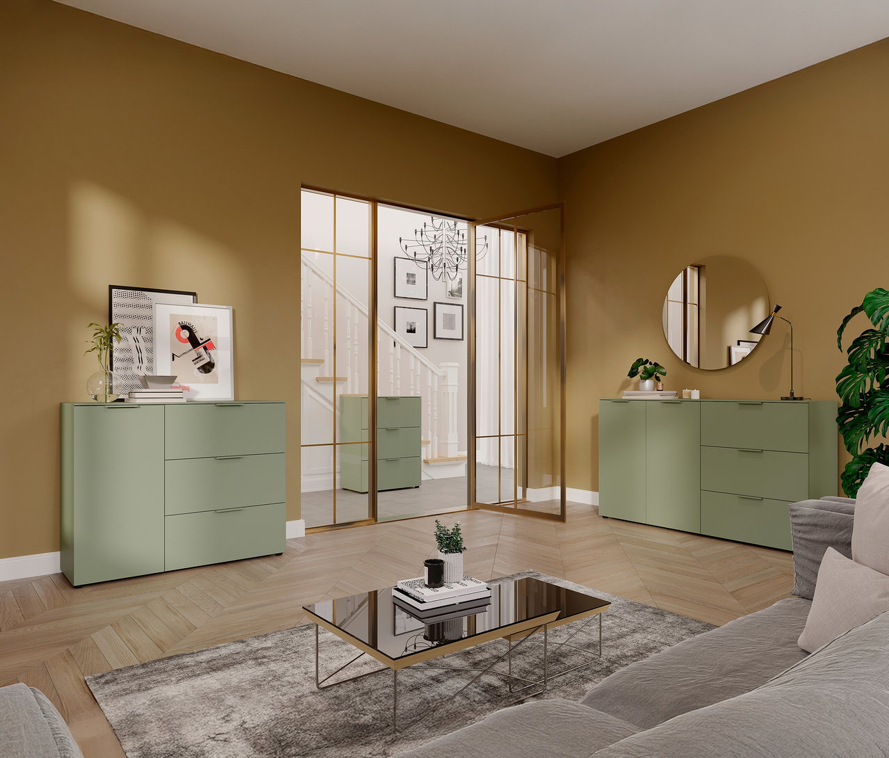 Wohnzimmer mit taupegrüner, kleiner »Savoca« Kommode, Glas-Couchtisch und teilweise sichtbarem grauem Sofa.