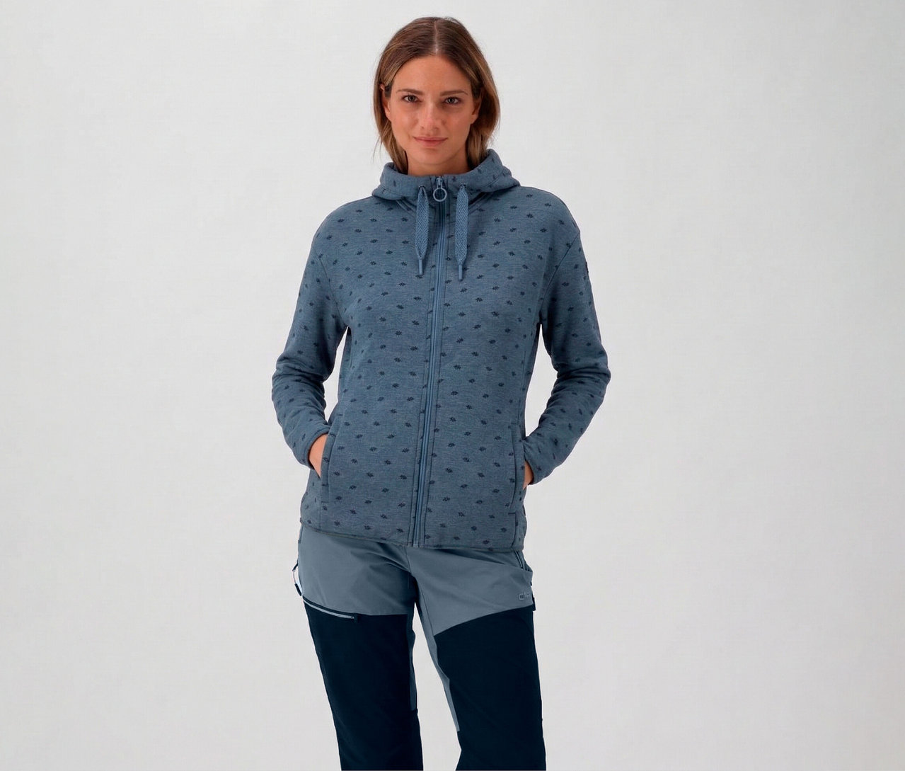 Frau mit blauer CMP Damen-Fleece-Jacke mit Kapuze und Händen in den Taschen.