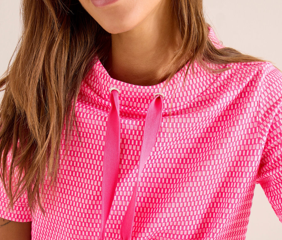 Lächelnde Frau mit langen braunen Haaren trägt ein kurzärmeliges, leuchtend pinkes CECIL Sweatshirt mit geometrischem Muster und Schalkragen mit Kordelzug.