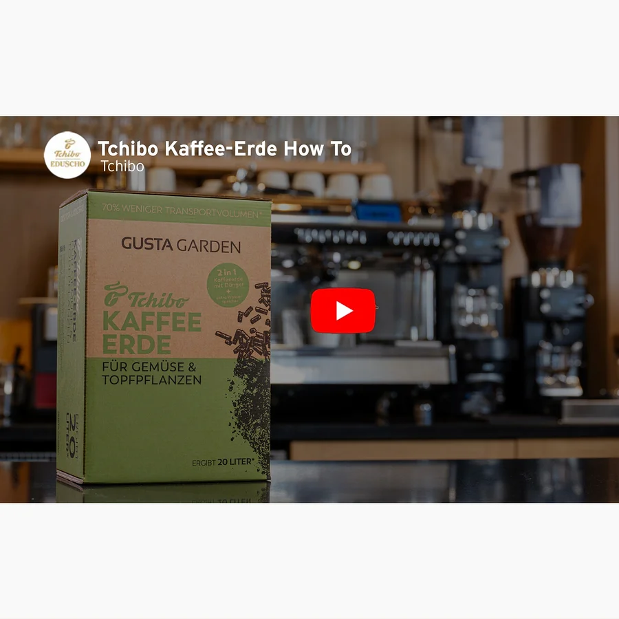 Eine Packung Tchibo Kaffee-Erde steht vor einer Kaffeemaschine. Ein roter Play-Button ist im Bild zu sehen.