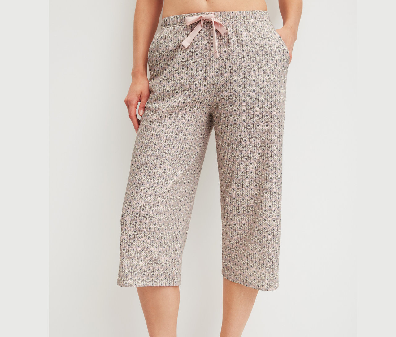 Nahaufnahme einer Frau, die gemusterte, knielange Pyjamahose mit rosa Kordelzug trägt.