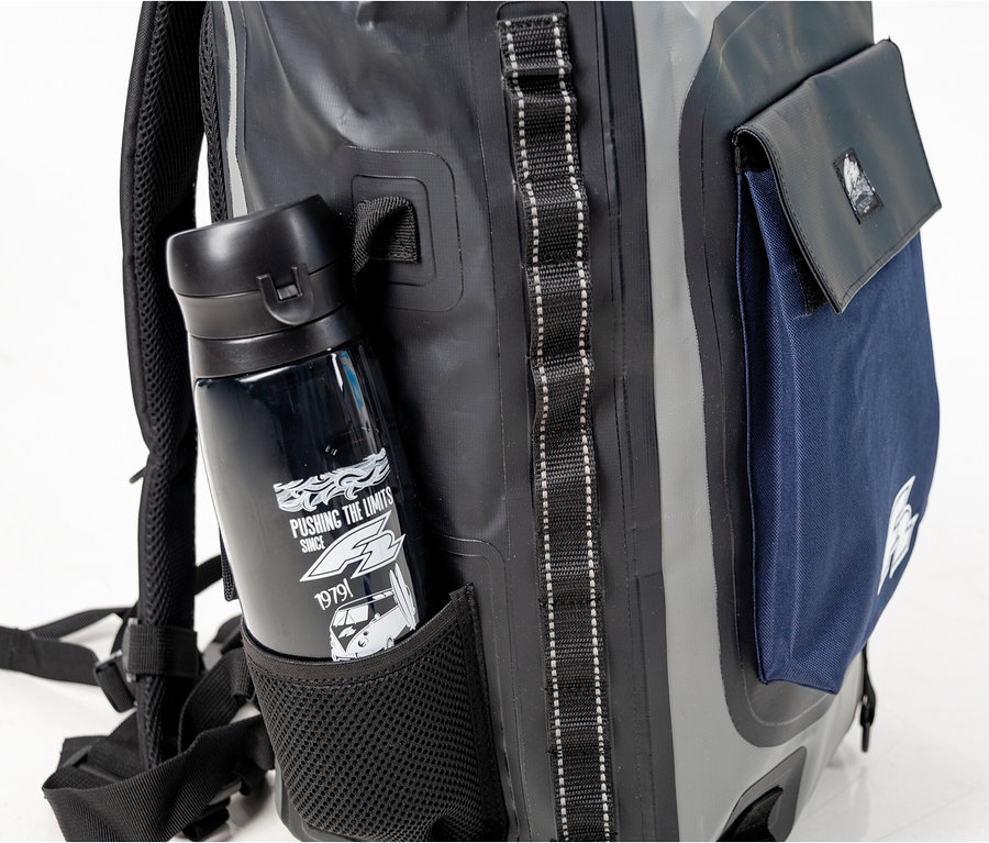 Eine schwarze Wasserflasche steckt in der Netztasche eines grauen Rucksacks mit blauer Tasche.