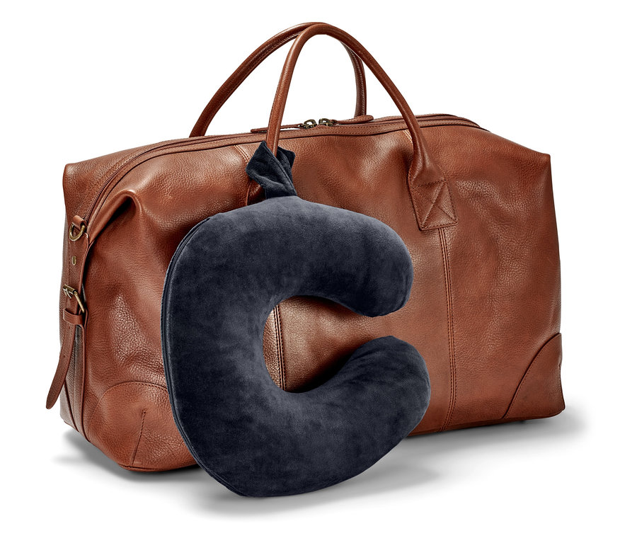 Ein dunkelblaues Nackenkissen hängt vor einer braunen Reisetasche.