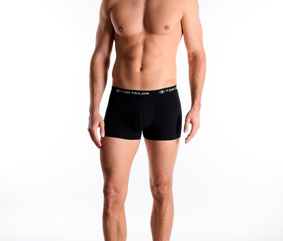 Mann steht barfuß da und trägt schwarze Boxershorts von Tom Tailor.