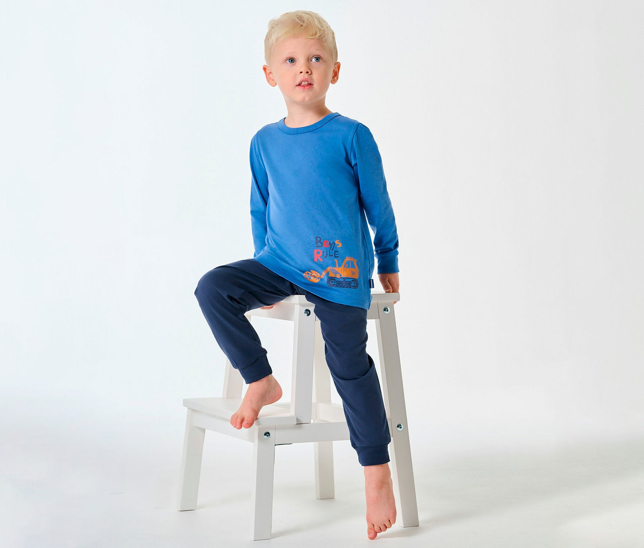 Blonder Junge im SCHIESSER langen Kinder-Pyjama sitzt barfuß auf einem Hocker.
