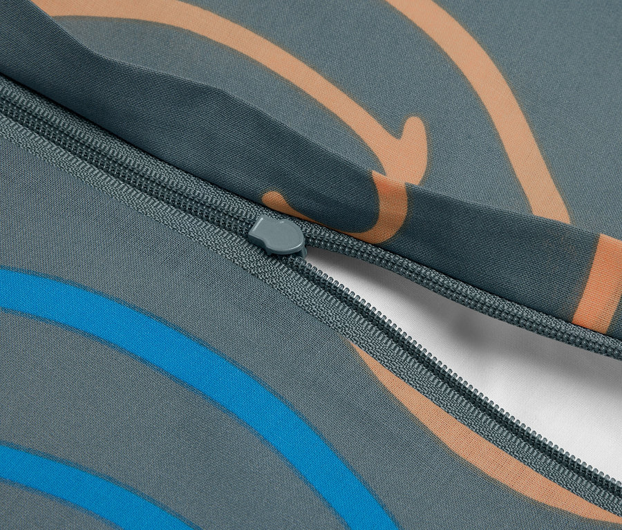 Nahaufnahme eines grauen Stoffes mit orangefarbenen und blauen Wellenmustern und einem teilweise geöffneten Reißverschluss, der weißen Stoff darunter zeigt.