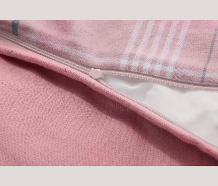 Nahaufnahme eines rosa Stoffes mit teilweise geöffnetem Reißverschluss. Der Stoff zeigt einen einfarbigen rosa Bereich und ein rosa Karomuster mit weißen und blauen Linien, das ein weißes Futter unter dem Reißverschluss enthüllt.