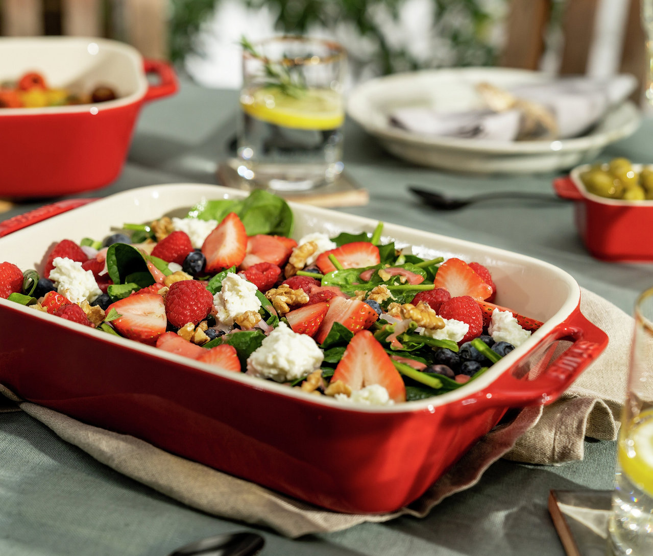 Kirschrote STAUB Auflaufform mit Salat aus Spinat, Erdbeeren, Himbeeren, Blaubeeren, Walnüssen und Käse. Weitere rote Auflaufformen im Hintergrund.