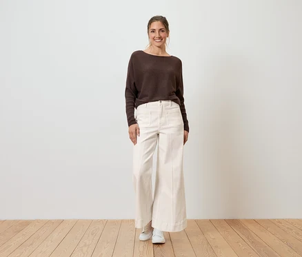 Eine lächelnde Frau trägt einen braunen Pullover und eine weiße Wide Leg Jeans im Fit „Viki“.