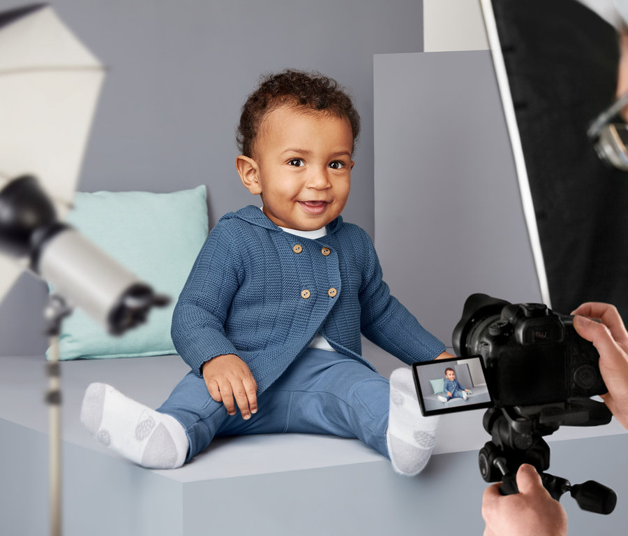 Lächelndes Baby sitzt und posiert in Strickjacke.