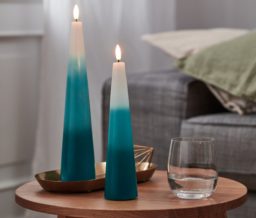 Zwei LED-Echtwachs-Kegelkerzen und ein Glas Wasser stehen auf einem Holztisch.