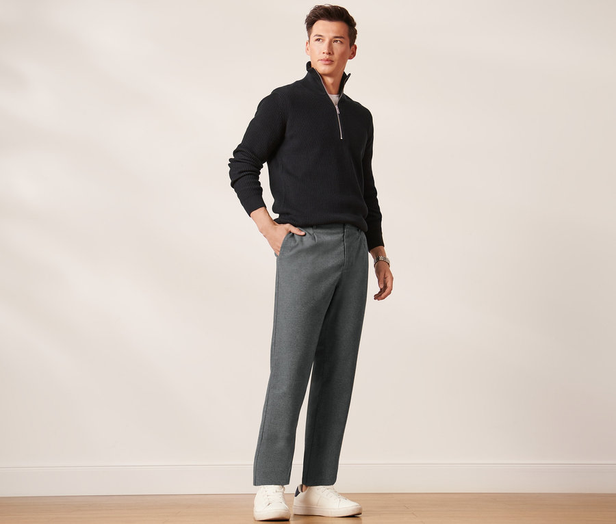 Mann posiert in schwarzem Pullover und grauer Comfort-Chino.