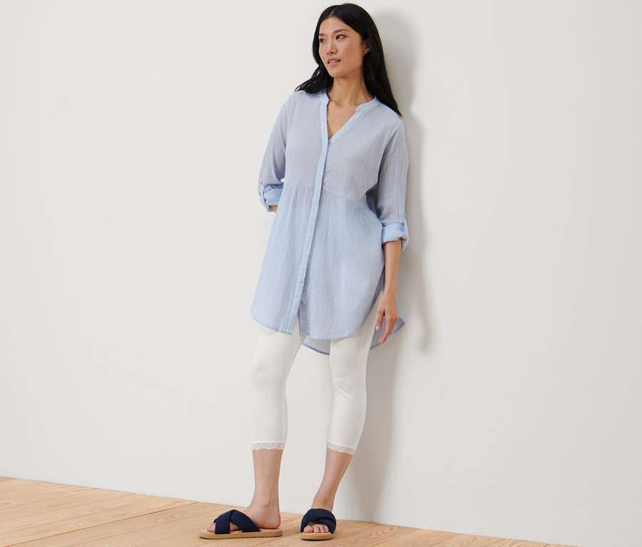 Eine Frau lehnt an einer Wand und trägt eine weiße 3/4-Leggings mit Spitzenborte.