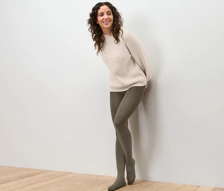 Frau lehnt an Wand und trägt Thermostrumpfhose und Pullover.