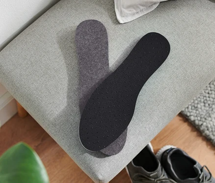 Zwei Thermo-Einlegesohlen liegen auf einer grauen Bank neben einem Paar grauer Schuhe.