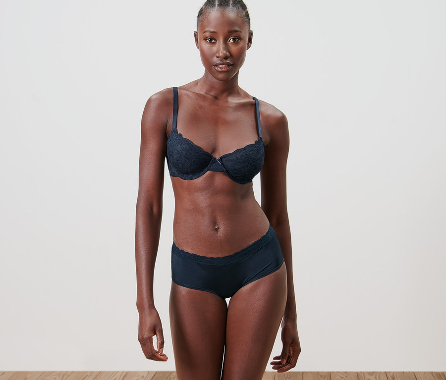 Schwarze Frau posiert in Unterwäsche. Sie trägt einen BH und 5 Pantys.