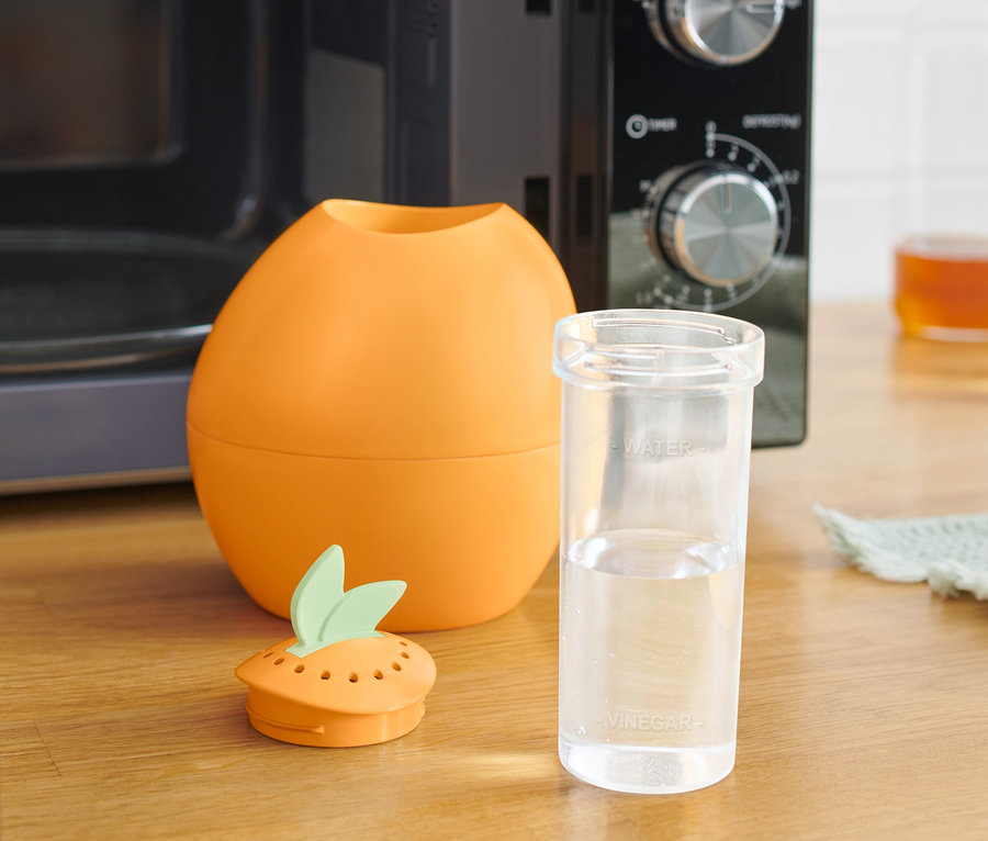 Oranger Mikrowellenreiniger neben einem Glas Wasser und einer Mikrowelle.